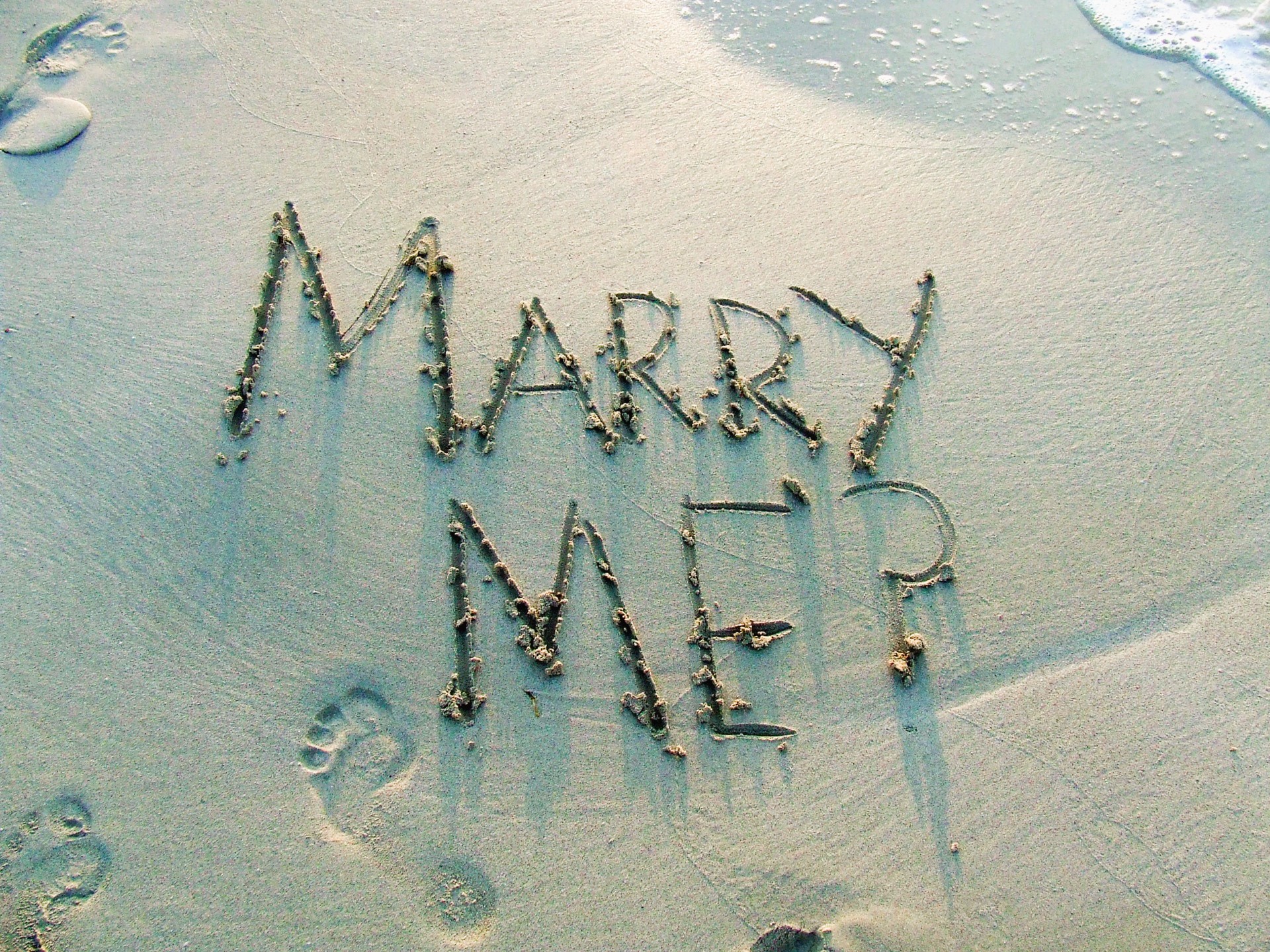Marry Me?; Marriage proposal written in the sand with the ocean gently lapping in