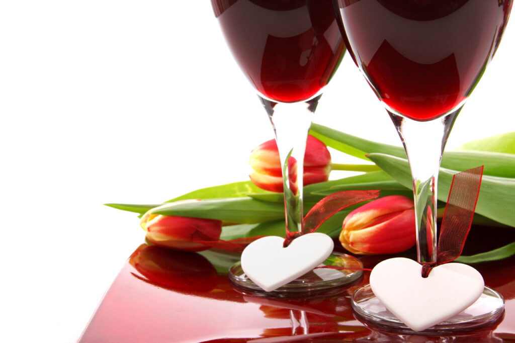 Celebration with two glasses of wine, white hearts and colourful tulips on white background